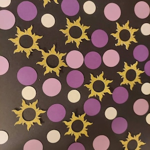 May include: A collection of purple and white paper circles and gold glitter sun cutouts on a black background.
