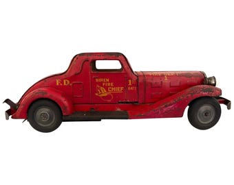 Op de afbeelding: Vintage rode speelgoed brandweerwagen met zwarte wielen. Het speelgoed heeft de tekst "F.D." en "SIREN FIRE CHIEF" op de zijkant. Een klassiek verzamelobject.