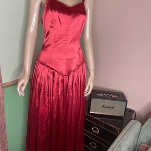 May include: A long, red satin dress with a sweetheart neckline and thin straps. The dress has a fitted bodice and a flowing skirt.