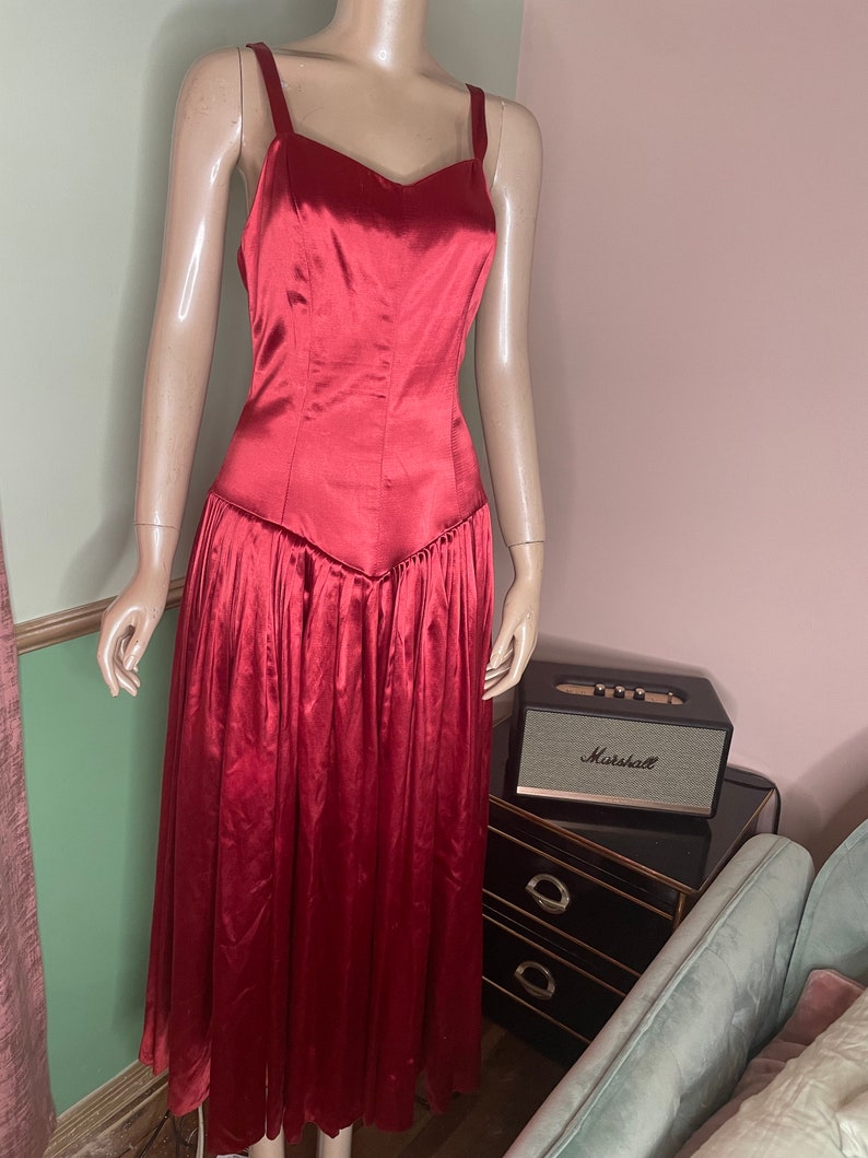 May include: A long, red satin dress with a sweetheart neckline and thin straps. The dress has a fitted bodice and a flowing skirt.