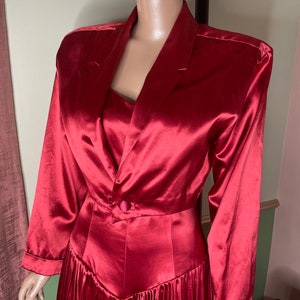 May include: A long, red satin dress with a fitted bodice and a flowing skirt. The dress has a single button closure at the waist and a V-neckline.