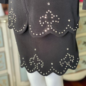 May include: Black skirt with a scalloped hem and rhinestone detailing. The skirt features a layered design with a matching top layer. Rhinestones are arranged in a floral pattern.