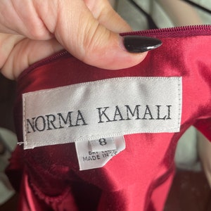 May include: A red satin dress with a white tag that reads "Norma Kamali" and "Size 8, Dry Clean, Made in USA."