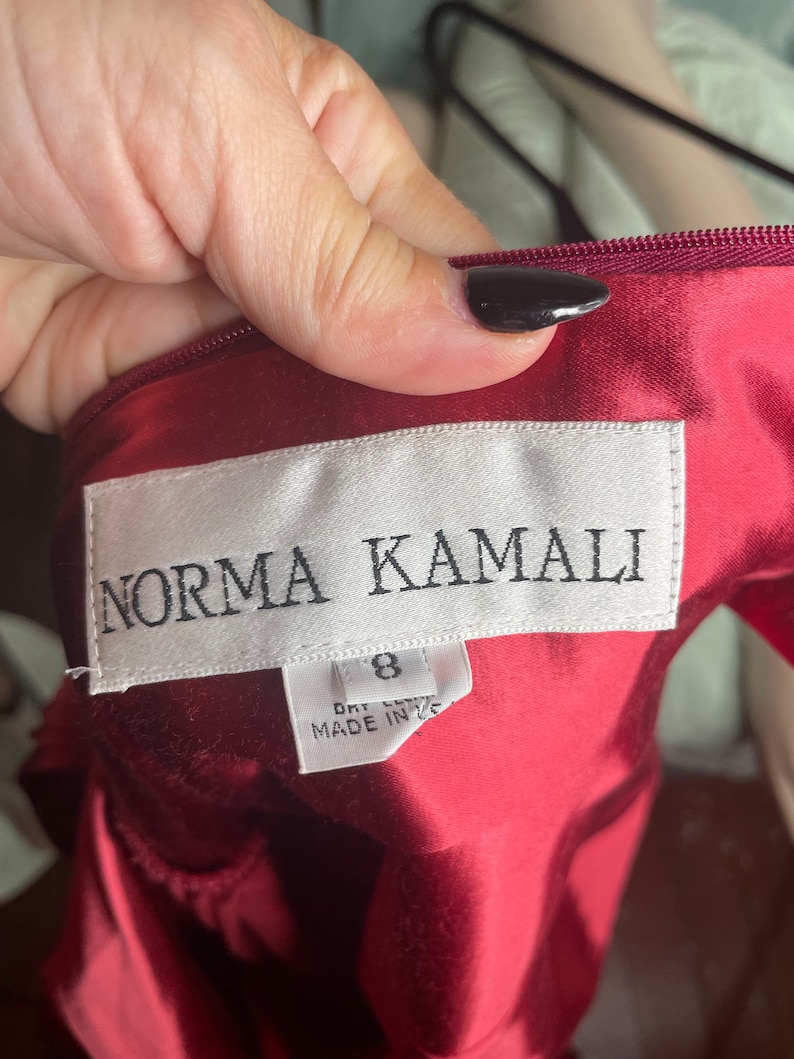 May include: A red satin dress with a white tag that reads "Norma Kamali" and "Size 8, Dry Clean, Made in USA."