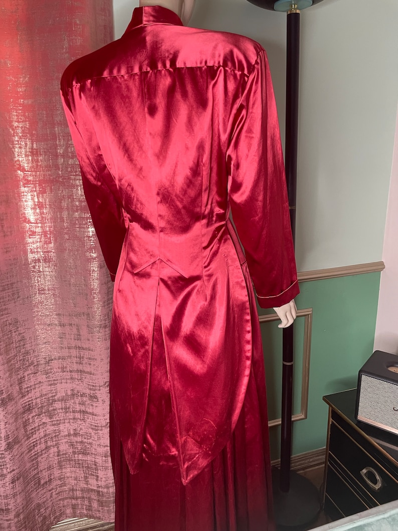 May include: A long, red satin dress with a high collar and a fitted bodice. The dress has a long, flowing skirt with a train.