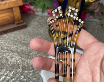 Puede incluir: Un peine para el cabello vintage con un patrón de carey y brillantes detalles de pedrería. El peine presenta un diseño en forma de abanico con múltiples púas y adornos decorativos, perfecto para añadir un toque de elegancia a cualquier peinado.