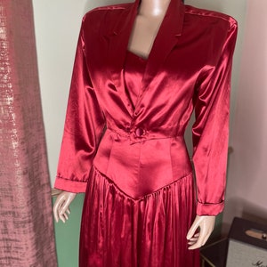 May include: A long, red satin dress with a fitted bodice and a flowing skirt. The dress has a button closure at the waist and long sleeves.