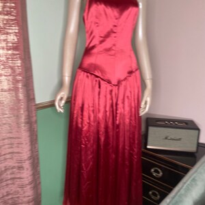 May include: A long, red satin dress with a sweetheart neckline and thin straps. The dress has a fitted bodice and a flowing skirt.