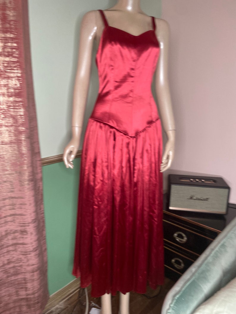May include: A long, red satin dress with a sweetheart neckline and thin straps. The dress has a fitted bodice and a flowing skirt.