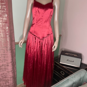 May include: A long, red satin dress with a fitted bodice and a flowing skirt. The dress has a sweetheart neckline and thin straps.