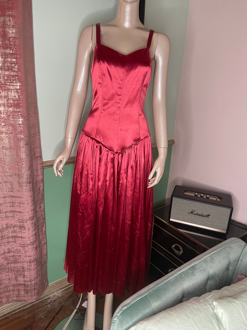 May include: A long, red satin dress with a fitted bodice and a flowing skirt. The dress has a sweetheart neckline and thin straps.