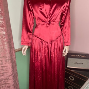 May include: A long, red satin dress with a fitted bodice and a flowing skirt. The dress has a blazer-style collar and a single button closure at the waist.