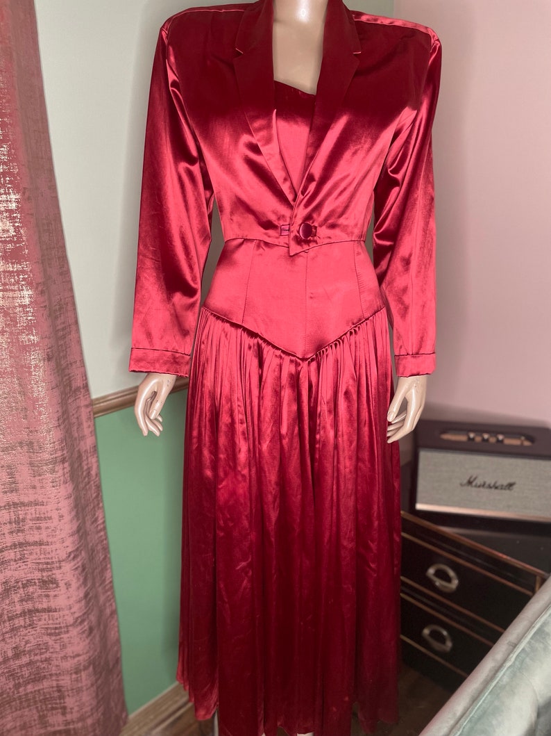 May include: A long, red satin dress with a fitted bodice and a flowing skirt. The dress has a blazer-style collar and a single button closure at the waist.