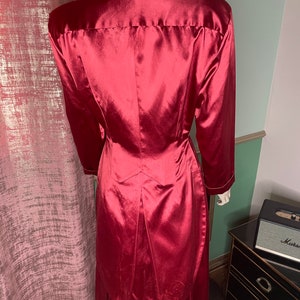 May include: A long, red satin robe with a high collar and long sleeves. The robe has a fitted bodice and a flowing skirt.