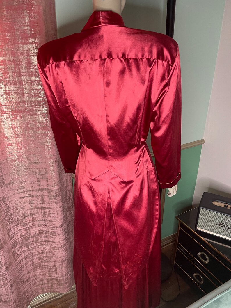 May include: A long, red satin robe with a high collar and long sleeves. The robe has a fitted bodice and a flowing skirt.