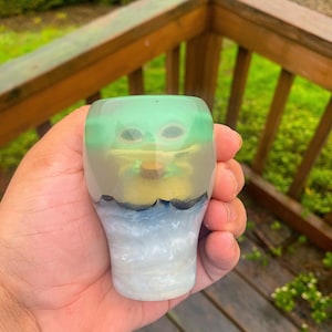 May include: A green, yellow, and blue resin figurine of a popular character from the Star Wars franchise. The figurine is encased in clear resin and has a white base.