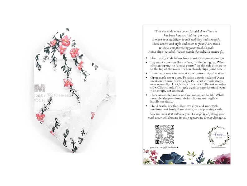 May include: White reusable face mask cover with a floral pattern of pink flowers and green stems. The mask cover has the text "M" and other text. The mask cover is designed to add style and color to your Aura mask.