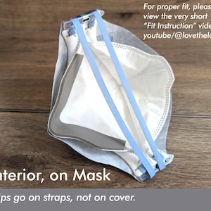 May include: A white and gray mask with light blue straps. The mask has the text "Interior, on Mask" and "Clips go on straps, not on cover." The image also includes the text "For proper fit, please view the very short "Fit Instruction" video at youtube/@lovethelook."