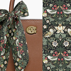 May include: A brown leather handbag with a decorative scarf tied to the handle. The scarf features a dark green background with a repeating pattern of birds, flowers, and berries. The bag has a gold-colored clasp.