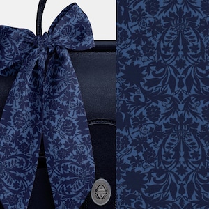 May include: A navy blue handbag with a matching patterned scarf tied to the handle. The scarf and the background pattern feature a floral design in shades of blue. The handbag has a silver clasp.