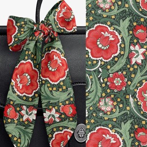 May include: A black leather bag adorned with a long, tied fabric ribbon featuring a repeating floral pattern. The print displays large red blossoms with white centers, intertwined with light green foliage and small yellow accents on a dark green background.
