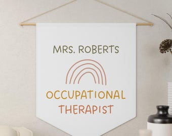 May include: A white banner with the text "MRS. ROBERTS" in green, a brown rainbow graphic, and the words "OCCUPATIONAL THERAPIST" in orange. The banner is suspended from a wooden rod with a string.