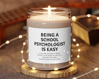 May include: A brown candle with a white label that reads "Being a School Psychologist is Easy. It's like riding a bike, except the bike is on fire. You're on fire. Everything is on fire."
