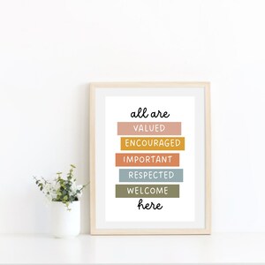 May include: A framed print with the text "all are valued encouraged important respected welcome here" in black lettering on a white background. The words are arranged in a vertical stack with each word on a different colored rectangle. The colors are peach, yellow, orange, blue, and green.