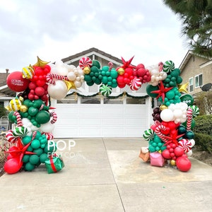 May include: A festive Christmas balloon archway in red, green, white, and gold. The arch features candy cane, star, and gift box accents. The text "POP FEST CO" is visible on the arch.