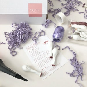 Peut inclure: Un kit de f&ecirc;te violet et blanc avec des ballons, un ruban, du ruban adh&eacute;sif et des instructions pour faire quelque chose de joli. Le kit comprend une carte avec le texte "Pr&ecirc;t &agrave; faire quelque chose de joli ?" et "Vos mat&eacute;riaux".