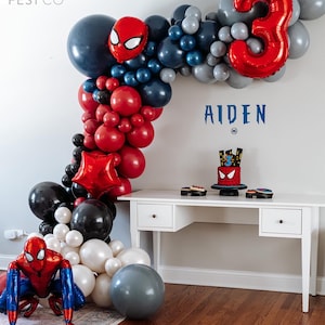 May include: A red, black, and white balloon arch with a Spiderman character balloon and a large red number 3 balloon. The arch is decorated with a Spiderman cake and the name Aiden.