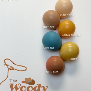 May include: A set of six balloons in various shades of brown, yellow, and blue. The balloons are arranged in a semi-circle with the text "POP FEST CO" at the top and "The Woody collection" at the bottom. The balloon colours are: Peachy Beige, Teddy Bear, Golden Mustard, Topaz Blue, Burnt Clay, and Honey.