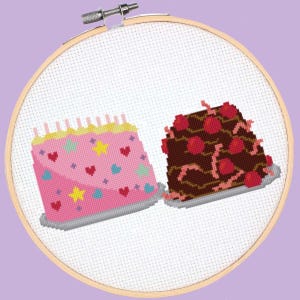 Może przedstawiać: Haft krzyżykowy przedstawiający dwa ciasta. Jedno jest różowe z sercami i gwiazdami, drugie czekoladowe z wiśniami. Haft umieszczony jest w drewnianym tamborku na jasnofioletowym tle.