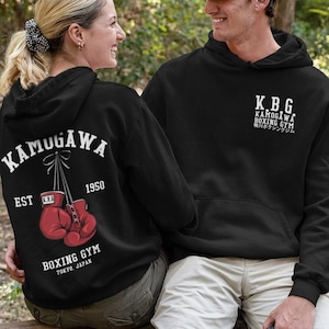 May include: Black hoodies with white text and red boxing gloves. The back of one hoodie says "Kamugawa Boxing Gym Tokyo Japan" with a graphic of boxing gloves. The other hoodie has "K.B.G. Kamugawa Boxing Gym" in white text.