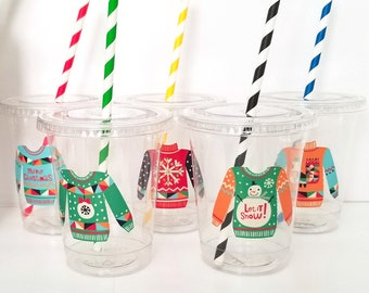 May include: Set of six clear plastic cups with colorful striped straws. Each cup has a different Christmas sweater design with festive colors and patterns. The designs include "Merry Christmas", "Let it Snow", and a snowflake pattern.