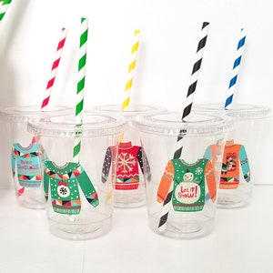 May include: Set of six clear plastic cups with colorful striped straws. Each cup has a different Christmas sweater design with festive colors and patterns. The designs include "Merry Christmas", "Let it Snow", and a snowflake pattern.
