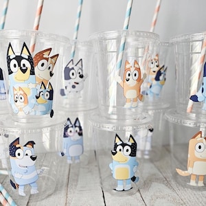 May include: Clear plastic cups with lids and straws, decorated with cartoon dog characters in various poses. The straws have blue and pink stripes. The cups are stacked on top of each other.