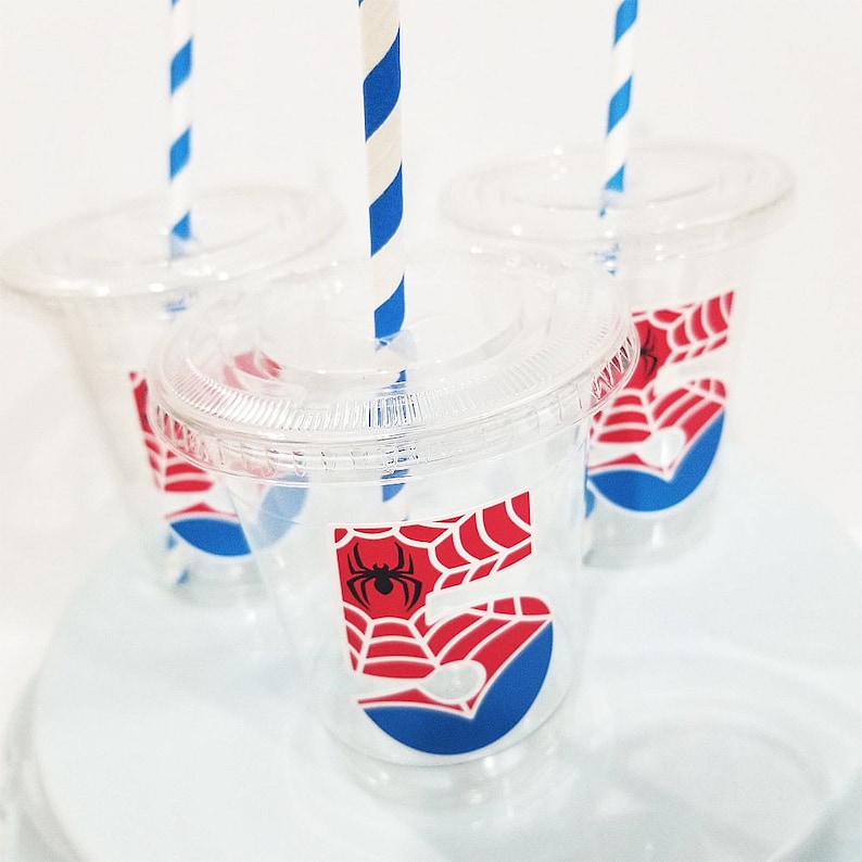 May include: Three clear plastic cups with red and blue Spiderman themed stickers. Each cup has a blue circle with a red number "5" and a black spider web design. The cups have white and blue striped straws.