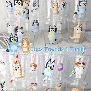 May include: Clear plastic cups with lids and straws, decorated with cartoon dog characters. The cups feature various dog designs, and the text "Cups Friends + Family" is visible. The straws have colorful stripes.