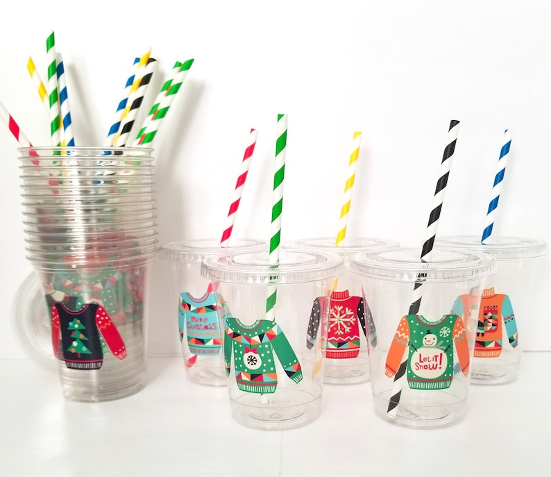 May include: Set of six clear plastic cups with colorful striped straws. Each cup has a different Christmas sweater design with festive colors and patterns. The designs include "Merry Christmas", "Let it Snow", and a snowflake pattern.