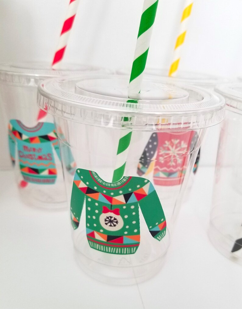May include: Clear plastic cups with festive Christmas sweater designs. The cups have green, red, blue, white, and black patterns. Each cup has a straw.