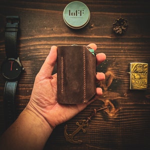 May include: A brown leather wallet with a stitched design. The wallet is being held in a person's hand. The wallet has a small label that says "lofi: leather goods".