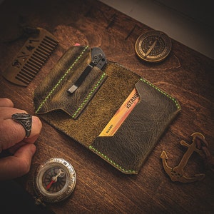 May include: A brown leather wallet with green stitching, a pocket for a small knife, and a card slot with a card that says "ISTANBUL" and "BALL LIGHT".