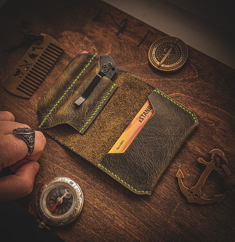 May include: A brown leather wallet with green stitching, a pocket for a small knife, and a card slot with a card that says "ISTANBUL" and "BALL LIGHT".