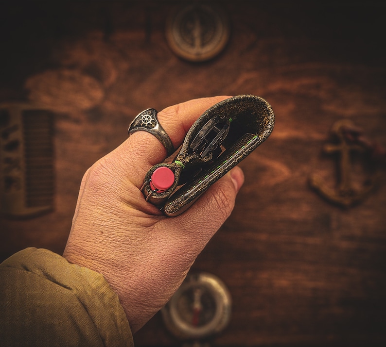 May include: A hand holding a brown leather wallet with a red button and a silver ring on the finger. The wallet is open and the inside is visible.