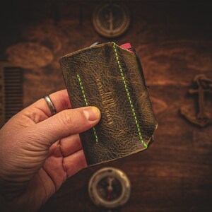 May include: A brown leather wallet with green stitching and the text "Leather Goods" embossed on the front.