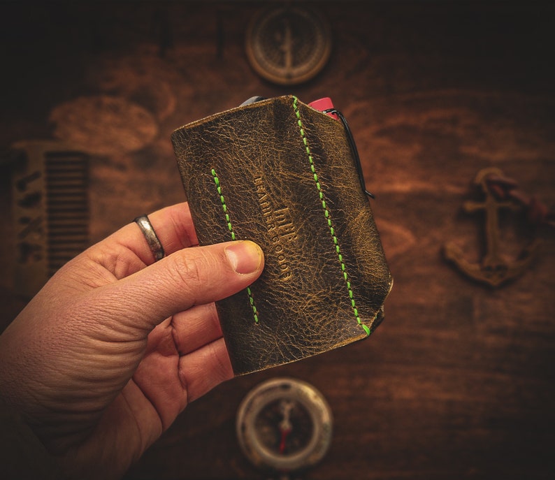 May include: A brown leather wallet with green stitching and the text "Leather Goods" embossed on the front.