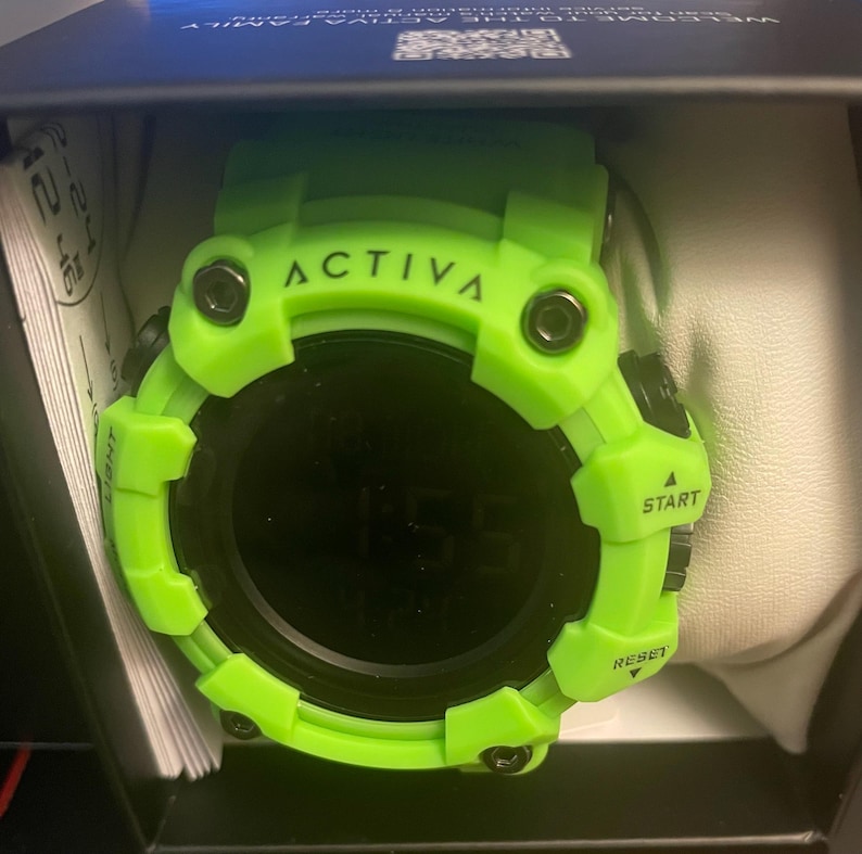 May include: A bright neon green digital watch with a round black face and a thick, rugged bezel. The watch features the brand name ACTIVA printed on the top, with buttons labeled LIGHT, START, and RESET on the sides. It is housed in a dark box.