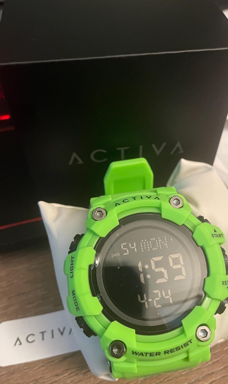 May include: A bright neon green digital watch with a round black face displaying the time 1:59, the date 4-24, and the day MON. The bezel features the text ACTIVA, LIGHT, MODE, START, RESET, and WATER RESIST with four visible silver-toned screws.
