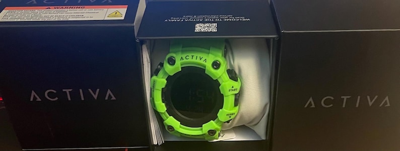 May include: A bright lime green digital watch with a round face and black accents, featuring the word ACTIVA printed on the bezel. The watch is housed inside a black box with the brand name ACTIVA printed in white on the front and side panels.
